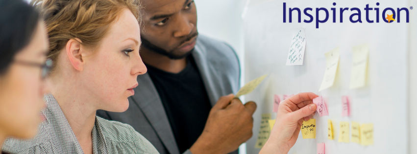 Three people sticking post it notes to a white board with the Inspiration logo in the top right of the image,